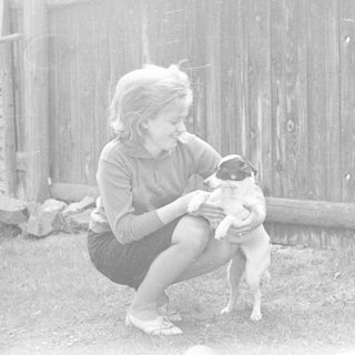A young girl kneeling, holding a small dog outdoors.