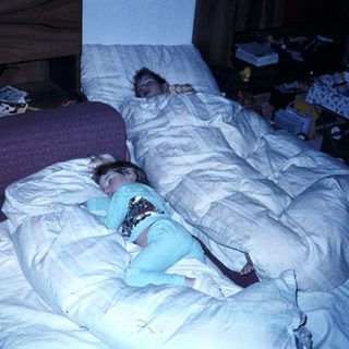 Two people sleeping in a cluttered bedroom.