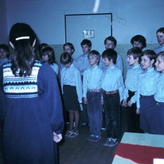 Children in school uniforms singing with teacher.