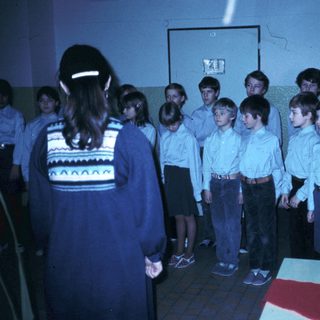 Children in school uniforms singing with teacher.