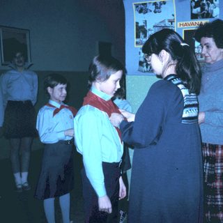 Girl receiving scout or guide neckerchief from adult leader.