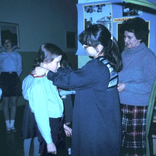 Girl receiving scout uniform patch from adult leader.