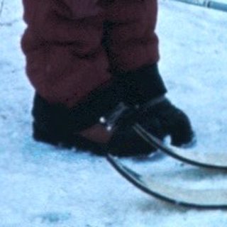 Two children holding skis by a snowy building.