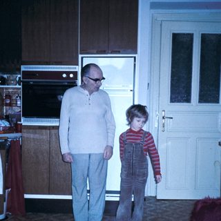 A man and child standing indoors near kitchen.