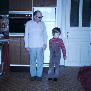 A man and child standing indoors near kitchen.