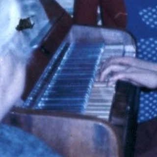 Family gathering with elderly woman playing piano, children and man listening.
