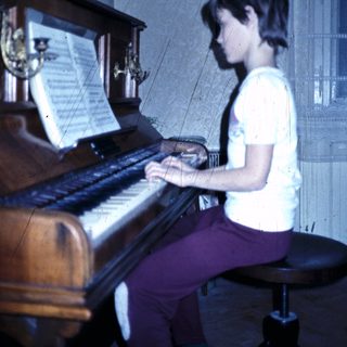 Young person playing a grand piano indoors.