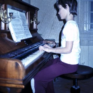 Young person playing a grand piano indoors.