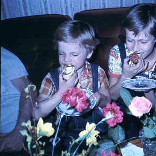 Two boys eating cake with flowers on table.