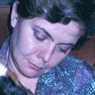 Woman cradling sleeping kitten indoors.