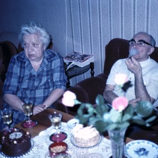Two elderly people celebrating with cakes indoors.
