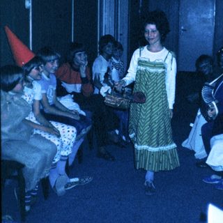 Group celebration with woman in traditional dress distributing treats.
