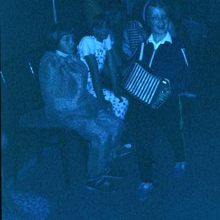 Group playing accordion in dimly lit indoor setting.
