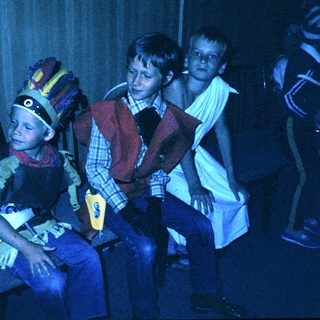 Children dressed in colorful costumes, seated indoors.