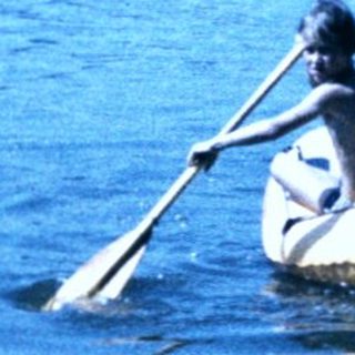 People paddling in an inflatable boat on calm water.