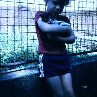 Boy hugging a cat near a fence.