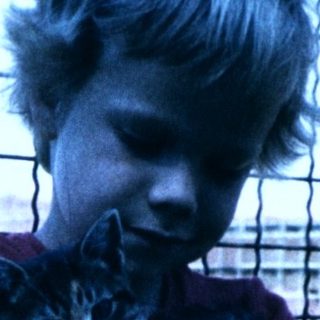 Boy hugging a cat near a fence.