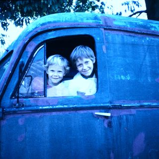Two children smiling from old truck window.