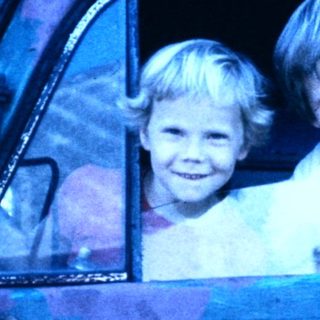 Two children smiling from old truck window.