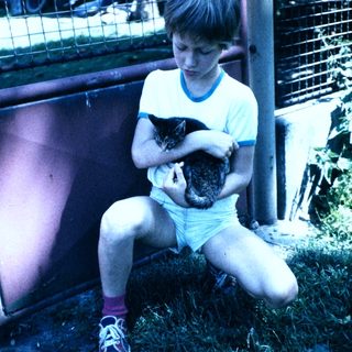 Boy holding two small cats outdoors.
