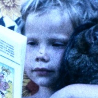 Child lounges in floral chair reading magazine.