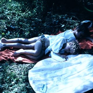 Child resting on blanket in natural setting.