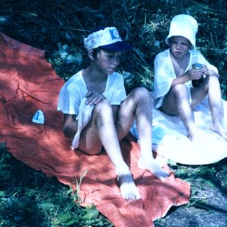 Two children sitting on blanket near water.