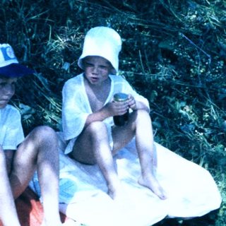 Two children sitting on blanket near water.