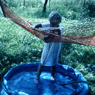 Child swinging on hammock above inflatable pool.