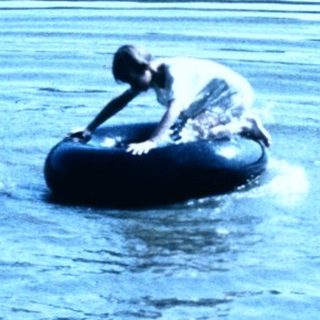Two people floating on inner tubes in calm lake.