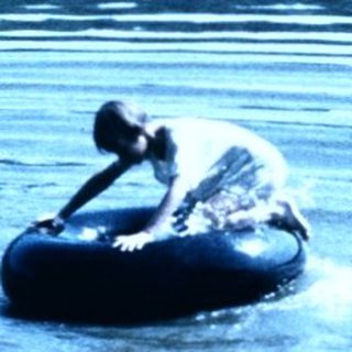 Two people floating on inner tubes in calm lake.