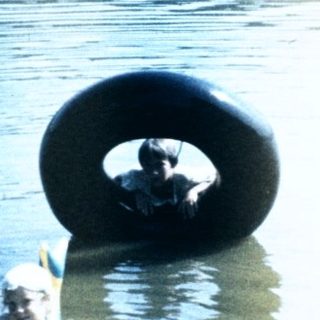 Person sitting in water with large tire.