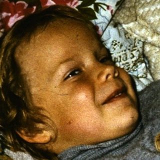 Toddler smiling while holding a gray cat.