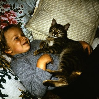 Toddler smiling while holding a gray cat.