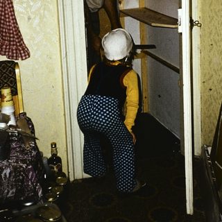 Two people carrying luggage through narrow hotel hallway.