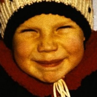 Child smiling on snow-covered ice with sled.