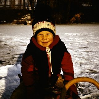 Child smiling on snow-covered ice with sled.