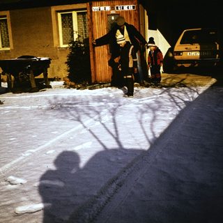 People shoveling snow outside a house at night.