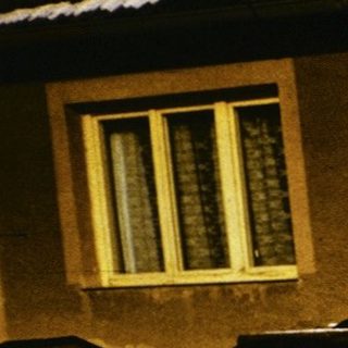 People shoveling snow outside a house at night.
