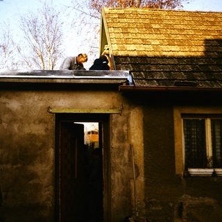 Two people repairing rustic roof on old building.