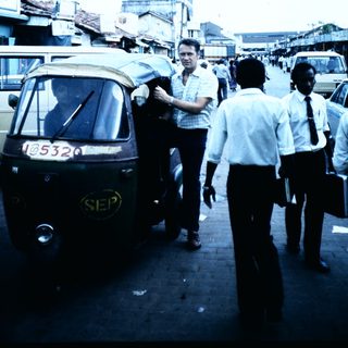 Busy urban street with auto-rickshaw and men in suits.