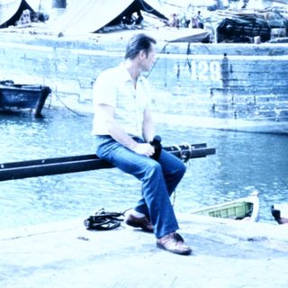 Man sitting by harbor near historic wooden boats.