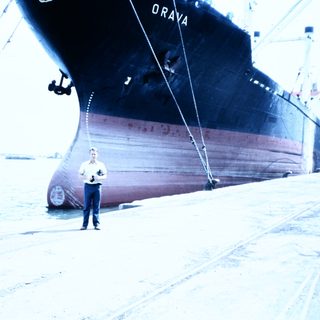 Man standing near docked cargo ship named "ORAVA."
