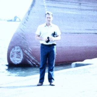 Man standing near docked cargo ship named "ORAVA."