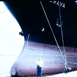 Man standing beside large docked cargo ship.
