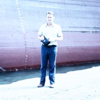 Man standing beside large docked cargo ship.