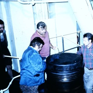 Group inspecting large industrial barrel onboard ship.