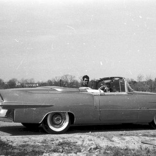 Vintage convertible car with two people, rural setting.