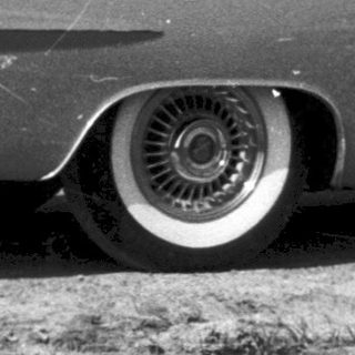 Vintage convertible car with two people, rural setting.