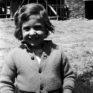 Smiling young girl in sweater outdoors near rustic buildings.